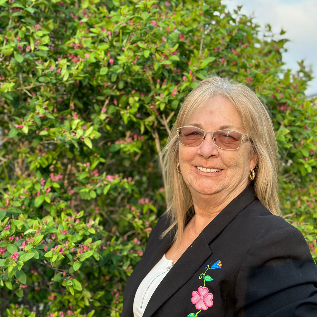 Val Uffelman, Chamber Treasurer, standing in front of a flowering shrub, smiling at the camera